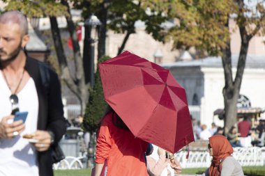 İstanbul, Türkiye - Kasım-06.2019: Meydanda kırmızı şemsiyeyle yürüyen kadın. Güneşten korunuyor. Turistler dolaşır. Sultanahmet Meydanı 'nda fotoğraf çekilmişti..
