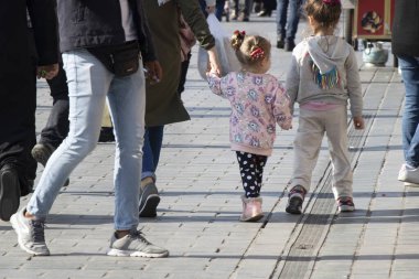 İstanbul, Türkiye - Ekim-27. 2019: Abla ve küçük kız kardeş el ele yürüyorlar. Caddenin ortasında, arkadan çekilmiş bir fotoğraf. Etrafta insanlar var..