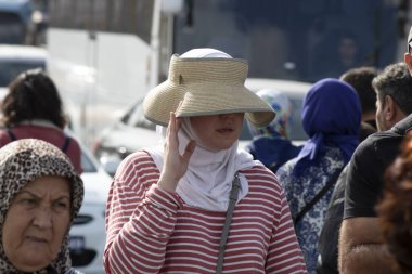 İstanbul, Türkiye - Ekim-27. 2019: Türbanlı kadın güneşten korunmak için özel bir şapka takıyor. Telefonla konuşuyor. Sokakta yürüyen insanlar.