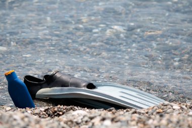 Sahilde çakıl taşları üzerinde yüzgeç ve güneş kremi. Güneşli bir günde çekilmiş..