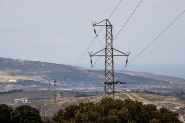 Elektrik hatları ve trafolar. Solda bir ağaç var ve hava bulutlu. Kışın çekilen bir fotoğraf. Gökçeada, Türkiye.