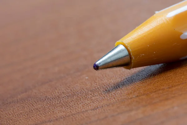 Ballpoint pen nib close-up. It is yellow and brown on the table. The ink is blue.