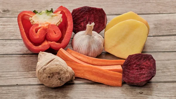 Sebzelerin vejetaryen menüsü: kırmızı biber, patates, sarımsak, havuç, pancar, zencefil, ahşap bir masanın üzerinde yatar.