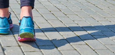 Havalı spor ayakkabılar ve siyah kotlar içinde şık kadın ayakları, bir gölge