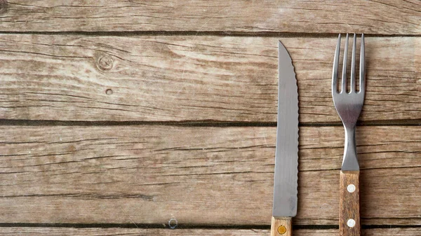knife  and fork with a wooden handle lies on an old oak tabletop, close-up, daylight, banner concept