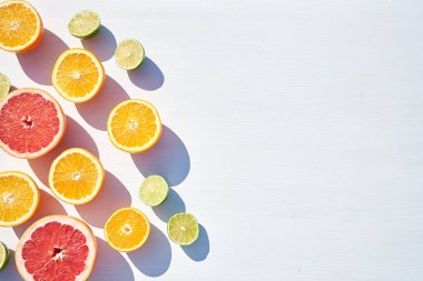 Olgun portakal, greyfurt ve kireç yarımları beyaz ahşap arka planda, yukarıdan sert güneş ışığı altında uzun renkli gölgelerle çekilmiş. Çok fazla geçmiş var..