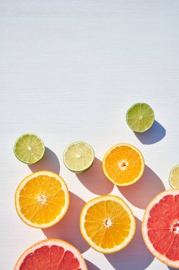 Beyaz ahşap zemin üzerinde olgun portakal, greyfurt ve kireç yarımları, yukarıdan sert güneş ışığı ve uzun renkli gölgeler. Çok fazla geçmiş var..