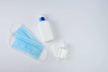 El dezenfektanının yanında beyaz antiseptik şişesi, antiseptik mendil ve beyaz akrilik masa üzerinde iki mavi ilaç maskesi.