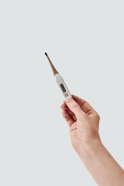 Beyaz arkaplana karşı 38.5 santigrat derecelik elektronik termometreyi tutan bir kadının dikey görüntüsü.