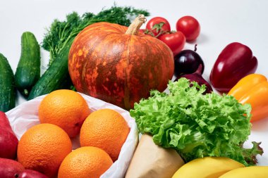 Bakkaliye: balkabağı, domates filizi, kırmızı soğan, kırmızı ve sarı dolma biber, salatalık, dereotu, portakal, kırmızı armut, marul, beyaz zemin üzerinde muz.