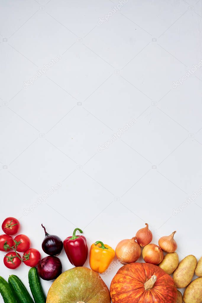 Groceries: two pumpkins, potatoes, sprig of tomatoes, red and yellow onions, red and yellow bell peppers, cucumbers on white background