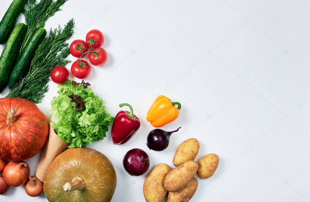 Groceries: two pumpkins, potatoes, sprig of tomatoes, onions, red and yellow bell peppers, cucumbers, dill, lettuce on white background, packed on the left