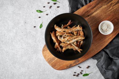 Kahverengi ahşap kesim tahtasındaki siyah mat tabağında kızarmış eritilmiş. Küçük sos kasesinde beyaz sos var. Açık gri arka planda duruyor.