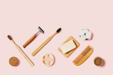 Pembe arka planda banyo aksesuarları. Doğal bambu diş fırçası, süngerler, pamuk çiçekler, tıraş fırçası. Düz yatış, üst görünüm.