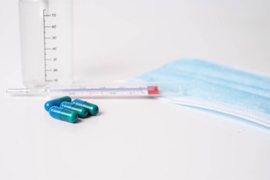 Tıbbi kapsüller ve beyaz arka planda termometre.