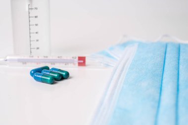 Tıbbi kapsüller ve beyaz arka planda termometre.