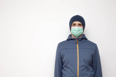 Beyaz arka planda yeşil koruyucu maskeli bir adam. Mavi ceketli, kapüşonlu bir adam..