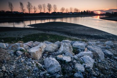 Drava nehrinin yanında gün doğumu. Yakından beyaz taşlar. Doğada cennet gibi bir gün doğumu. Güneş doğarken çekilen manzara fotoğrafı sağ üst köşede, beyaz taşlar önde ve nehir ortada. Hırvatistan.