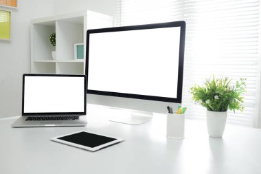 Bilgisayar, klavye, fare, akıllı telefon, kalemler, kaktüs ve ağaç vazolarının hepsi ahşap masada.