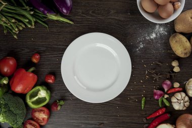 Taze organik sebze ve boş beyaz plaka etrafında lezzetli vejetaryen yemek için baharat maddeler, üst görünümü. Sağlıklı veya diyet gıda kavramı.