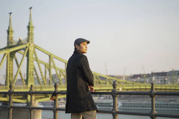 a stylish young man with a bridge, sea and blue sky as his background