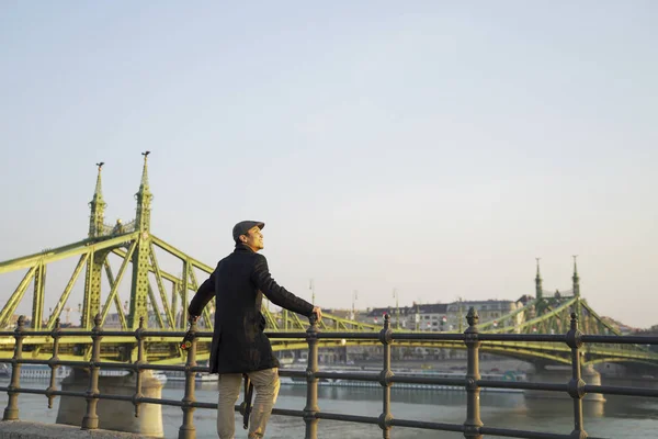 a stylish young man with a bridge, sea and blue sky as his background