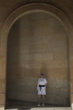 Bej tesettürlü şık Asyalı kadın Granada, İspanya 'da bulunan Alhambra' nın büyük, eski süslü kapısının önünde duruyor.