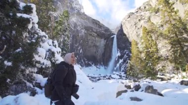 Genç Müslüman kaşif Yosemite şelalesinin etrafındaki kar manzarasının tadını çıkarıyor.