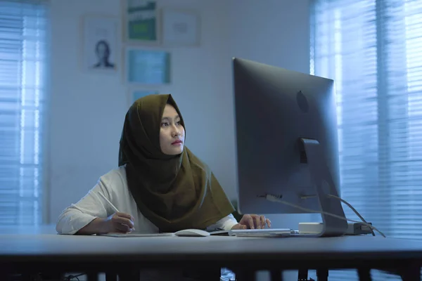 Beautiful Asian Muslims wearing green headscarves working from home in a modern interior design workspace with the warm blue light from the windows