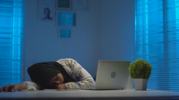 若いの柔らかい焦点黒いスカーフを身に着けている美しいアジアのイスラム教徒は 窓から暖かい青の光と現代的なインテリアデザインのワークスペースで夜に家から働くときに疲れと眠くなる — ストック動画