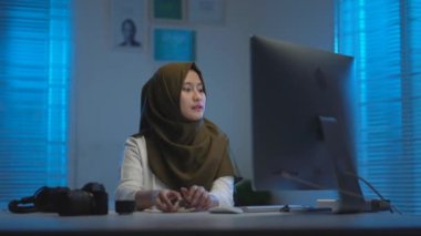 Koyu renk başörtüsü takan genç Asyalı Müslümanların yumuşak odak noktası, sıcak mavi ışıkla modern iç tasarım çalışma alanlarında gece evde çalışırken işini tamamladı.