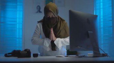 Genç Asyalı Müslüman kadınların nazik odak noktası koyu renk başörtüler takarak maskeler takarak, geceleri evde çalışırken sıcak mavi ışık ile modern bir iç tasarım çalışma alanında
