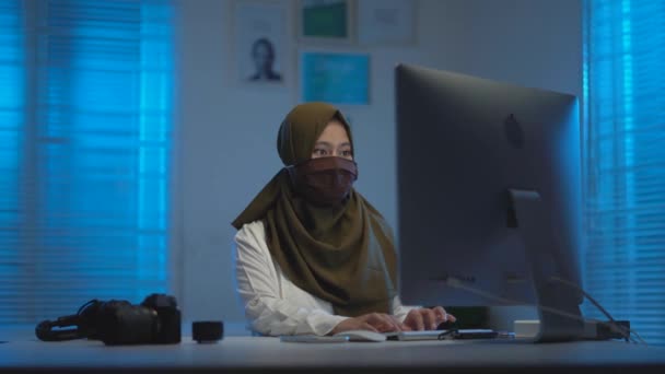 若いイスラム教徒アジアの女性は暖かい青の光と現代的なデザインのコワーキングスペースで夜に自宅から仕事中に咳 — ストック動画