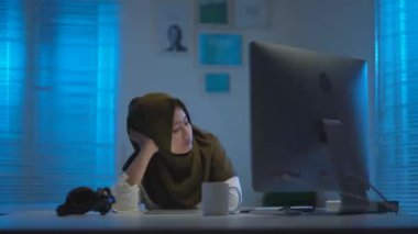 Genç ve güzel Asyalı Müslümanların koyu renk başörtüleri takıp geceleri evde çalışırken yorgun ve uykulu oldukları modern bir iç tasarım çalışma alanında sıcak mavi ışıkla çalışmalarının odağı.