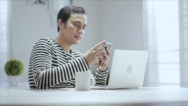 Обычный Азиатский Молодой Человек Работающий Дома Своим Ноутбуком Своим Гаджетом — стоковое видео