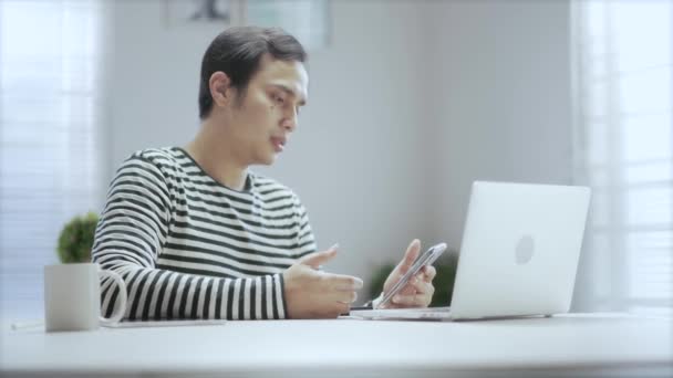 クリーンでモダンなデザインのワークスペースで一日中家で働いている間 カジュアルなアジアの若者がビデオ通話で何かを説明します — ストック動画