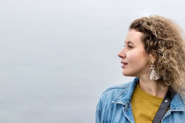 Kıvırcık saçlı genç bir kadının portresi. Başka tarafa bakıyor. Hayal görüyor, açık havada, profil görüşlü..