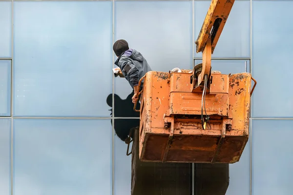 Άνδρας μη αναγνωρίσιμος εργαζόμενος που καθαρίζει τα παράθυρα ενός κτιρίου που στέκεται πάνω σε γερανό, σε εξωτερικούς χώρους — Φωτογραφία Αρχείου