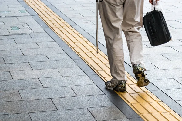 Blind unrecognizable person walking on a tactile paving path, rear view, outdoors