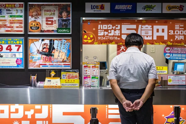 Homem japonês com as mãos nas costas olhando carrapatos de loteria no Hiroshima Bus Center no Japão . — Fotografia de Stock