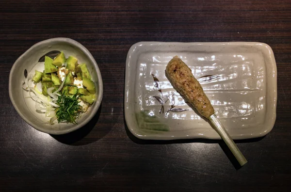 Japanese avocado salad and tsukune chicken stick on ceramic plates. — Stock Photo, Image