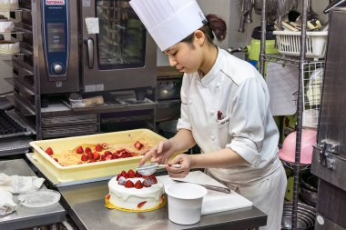 Japon bir kadın pasta şefi pudra şekerle pasta süslüyor..