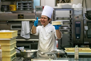 Japon bir erkek pasta şefi mutfaktaki süslemek için elinde yuvarlak pasta tutarken gülümsüyor..