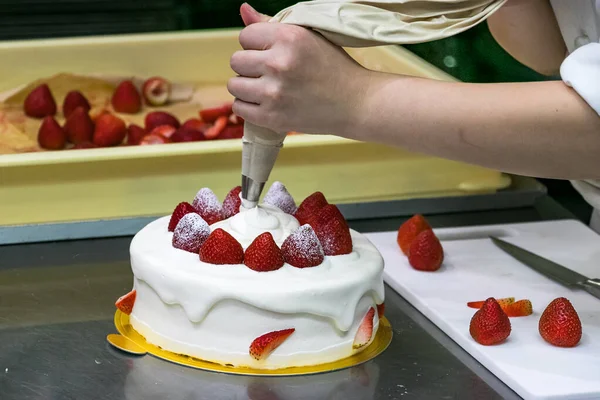 Female pastry chef hands, decorating a strawberries cake with a cream sleeve