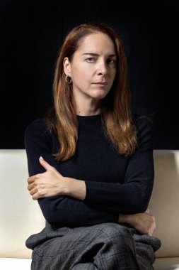 Olgun kadın 45-50 yaşlarında, ciddi, düşünceli, siyah arka planda çapraz kolları olan bir kamera..