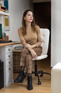 Olgun bir kadının portresi 45-50 yıl düşünceli bakışlar, evinde bir masanın yanında oturuyor..