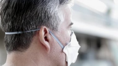 Olgun bir adamın portresi - doktor, koruyucu bir maske takıyor, başka tarafa bakıyor, düşünüyor, endişeleniyor..