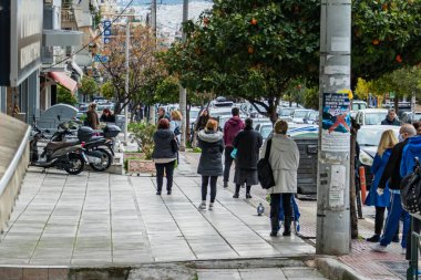 İnsanlar dışarıdaki süpermarkete girip güvenli mesafeyi korumayı bekliyor. Atina, Yunanistan.