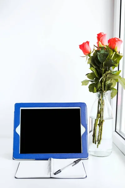 tablet, notepad and a bouquet of flowers on the desktop by the window, place for text