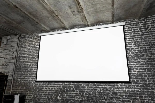 Angle view of white projector screen on grey brick wall — Stock Photo, Image